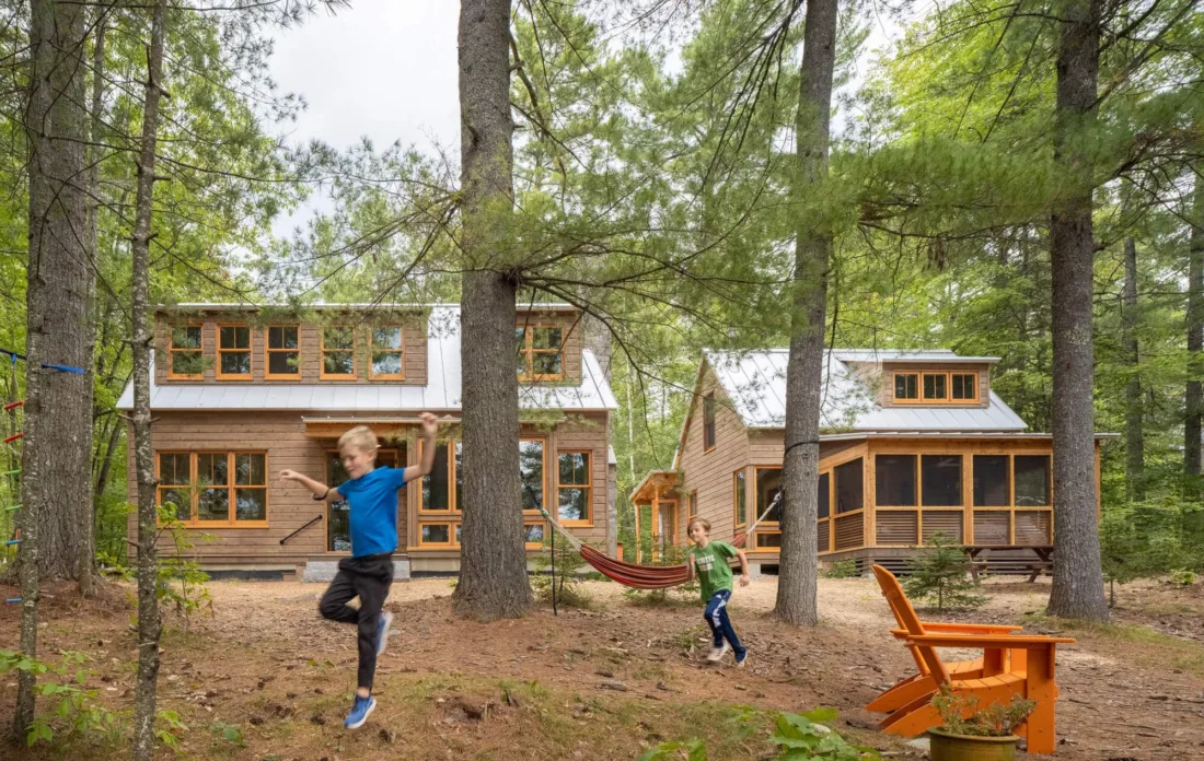 Canoe Camps’ twin cabins tucked among tall pines, with kids playing out front and a hammock strung between trees for laid-back lounging