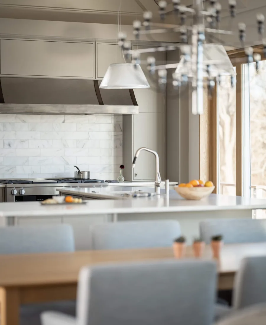 Modern kitchen with marble backsplash, stainless steel appliances, and pendant lights, viewed from a dining area—perfect inspiration for homes in Maine.