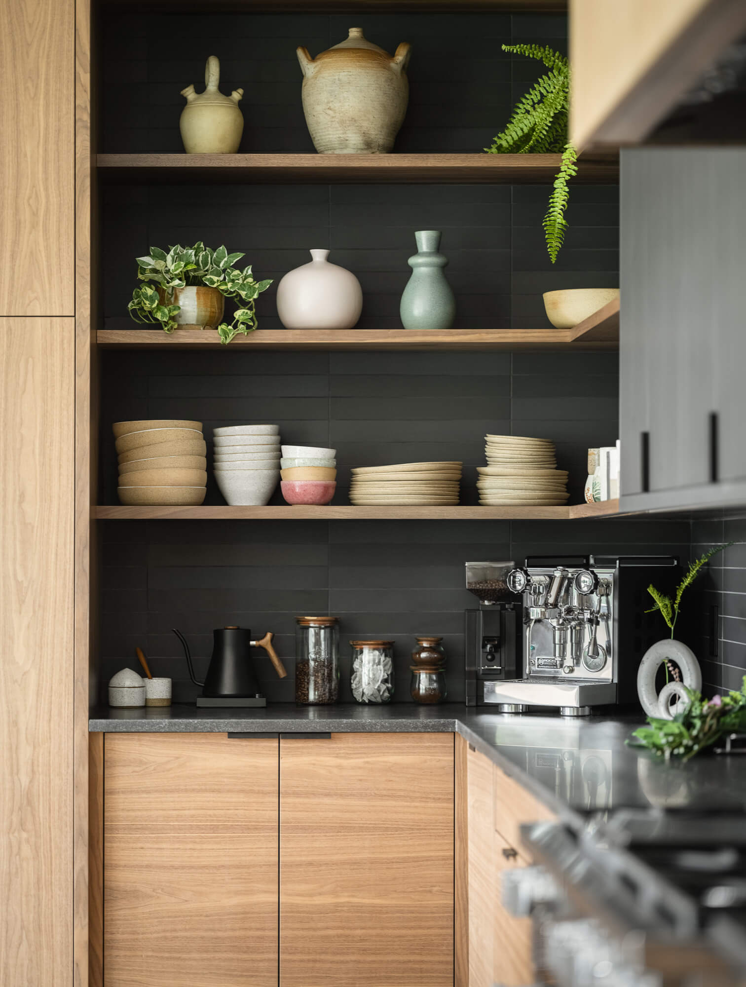 Close-up of open shelving in a custom-designed kitchen, featuring handcrafted pottery and sleek black backsplash, in a luxury home in New Gloucester, Maine