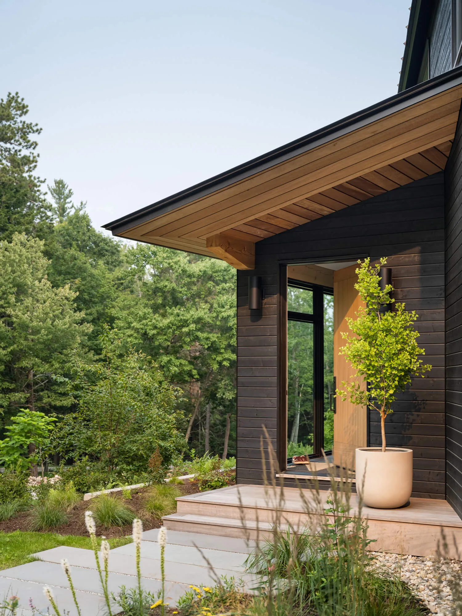 Architectural detail of the front entryway of a high-end custom home in New Gloucester, Maine, showcasing sleek black siding and a welcoming landscaped pathway