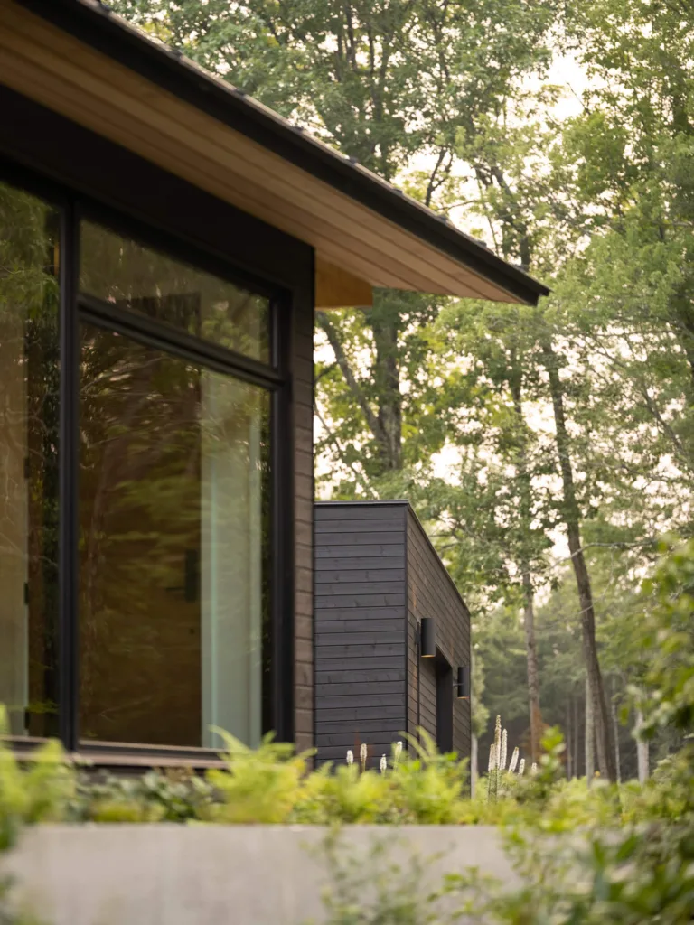 Modern architectural detail of a design-build home in New Gloucester, Maine, featuring clean black siding and lush landscaping for a high-end finish