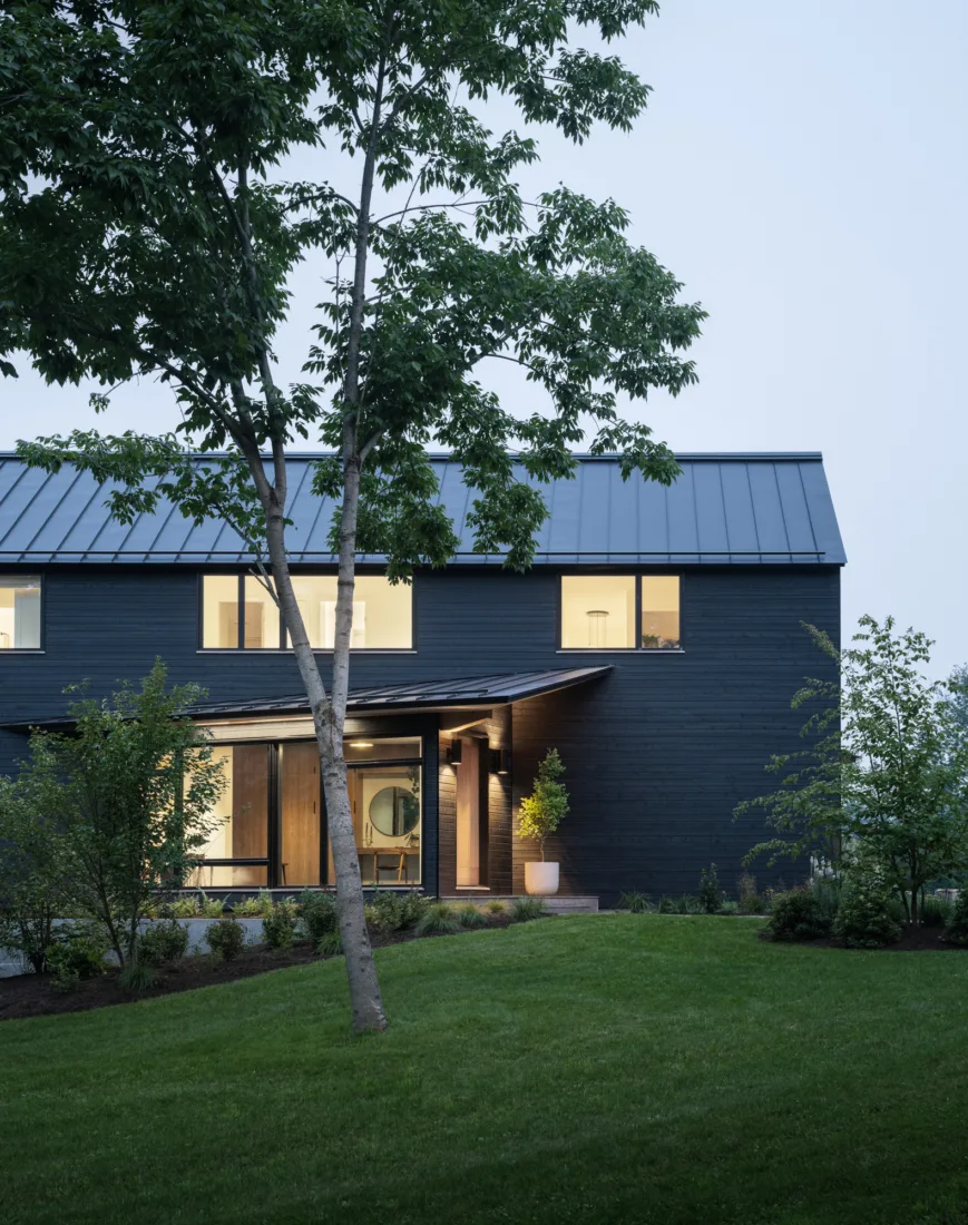 Modern black house with large windows and a welcoming front entrance surrounded by lush landscaping and trees