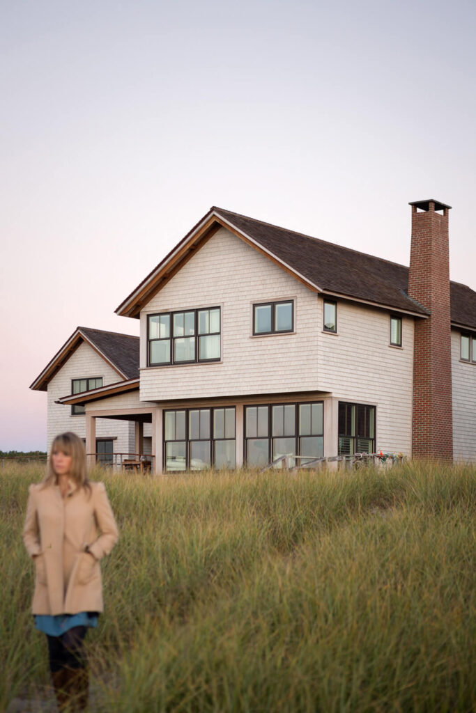 A woman walking down a path away from the Cast On house. The path has long grass and the home is off in the distance