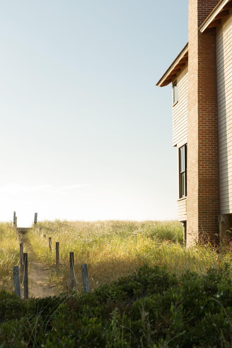 Walkway next to Cast On home looking towards the ocean with sand and long grass and a chimney