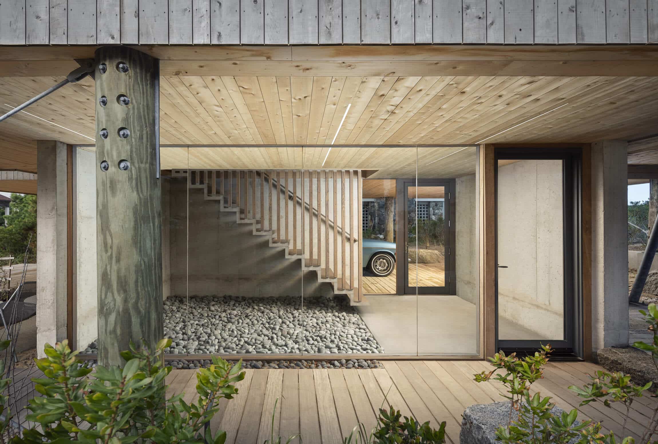 In the dunes entry way with a wood walkway, large glass windows, and a stairway leading up into the home