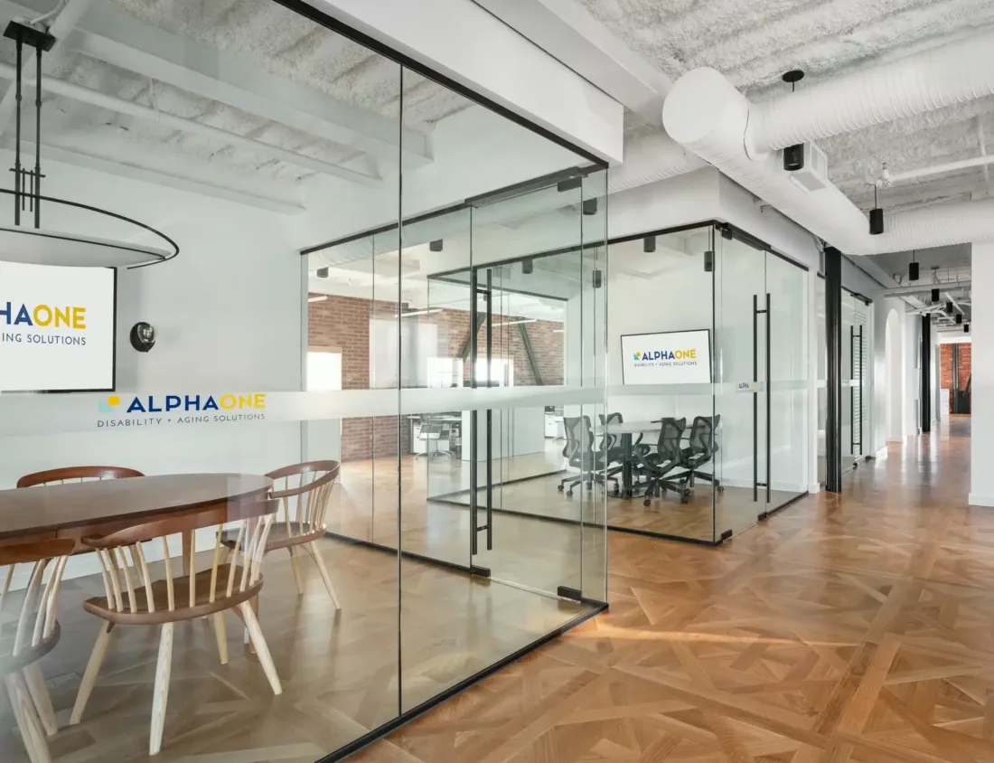 Alpha One Office’s modern interior features glass-walled conference rooms, natural wood floors, exposed ceilings, and bold branding throughout