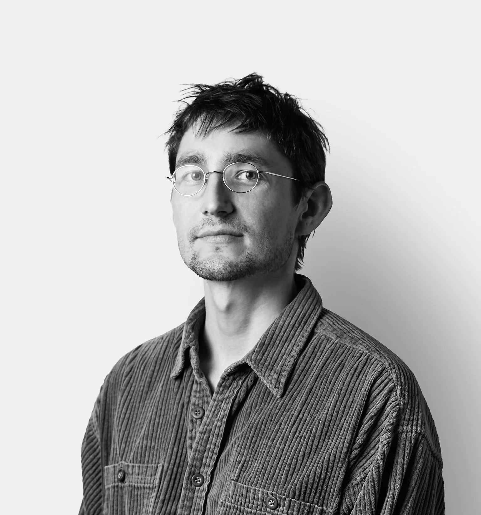 A man with short dark hair, glasses, and a striped button-up shirt poses against a plain white background.