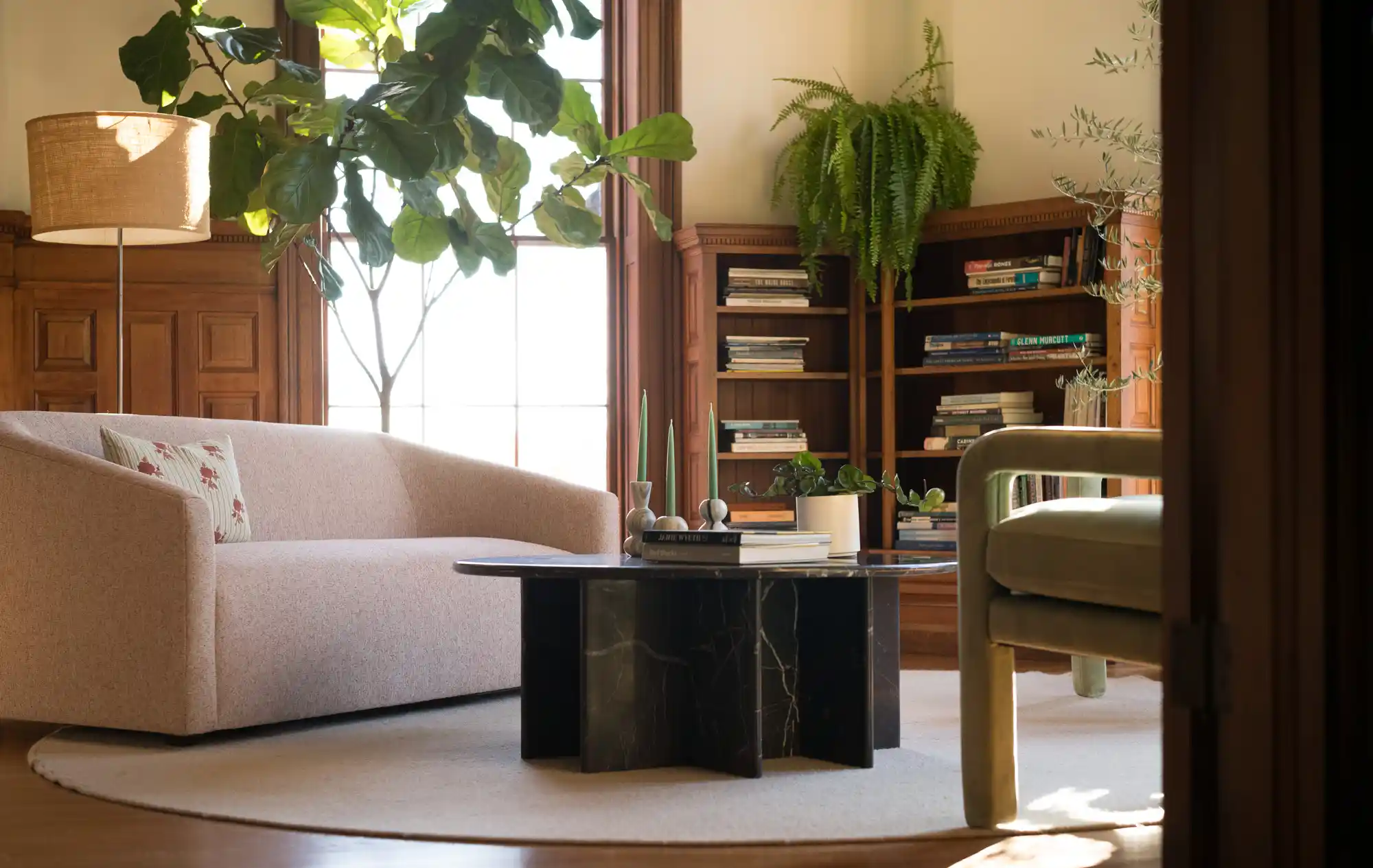 Interior seating area with modern furniture and restored wood paneling, featuring plants, a black marble table, and a beige sofa at Woodhull's renovated office.