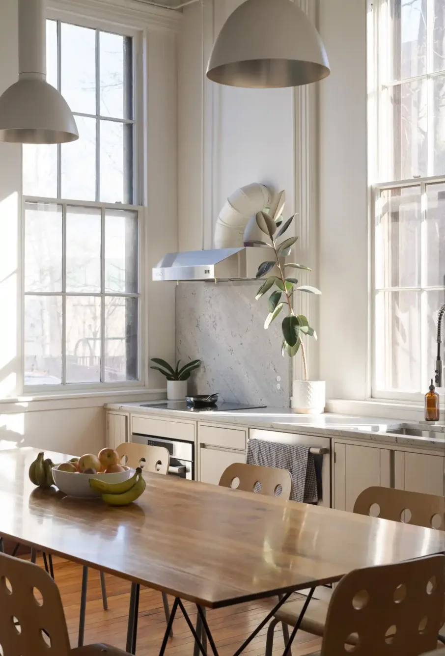 Office kitchen with white cabinetry, stainless cooktop, and a dining table with fresh fruit, offering a light-filled, functional space for Woodhull employees.