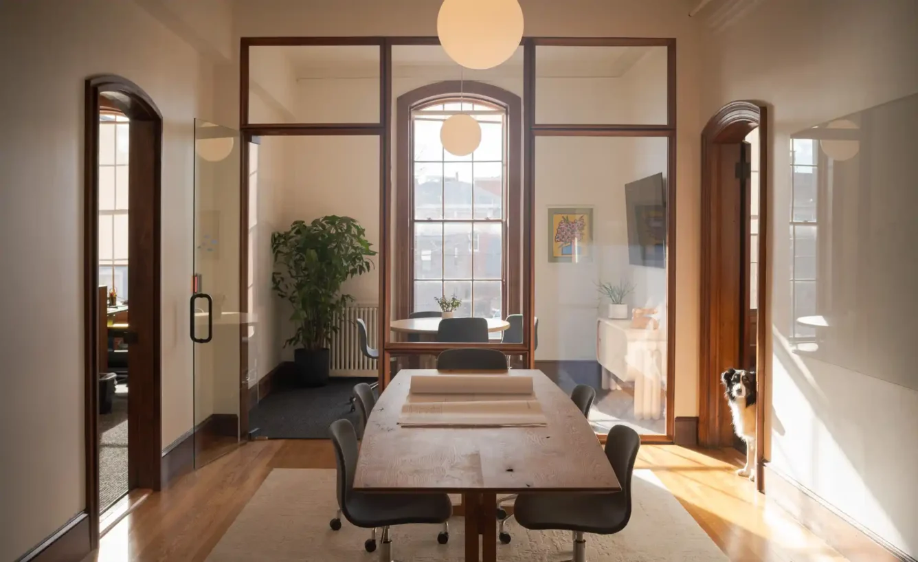 Meeting room in Woodhull’s office with glass panels and historic wood trim, featuring a round table, chairs, and ample light from floor-to-ceiling windows.