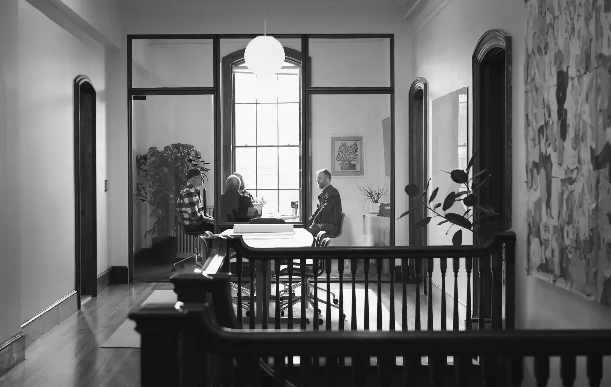 Black and white photo of a Woodhull meeting room with glass panels and wood trim, showing a collaborative meeting space with a round table and engaged employees.