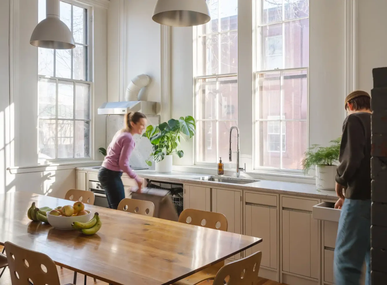 Office kitchen with white walls and historic wood trim, featuring two employees using the space. Tall windows bring natural light into the modern yet historic kitchen.