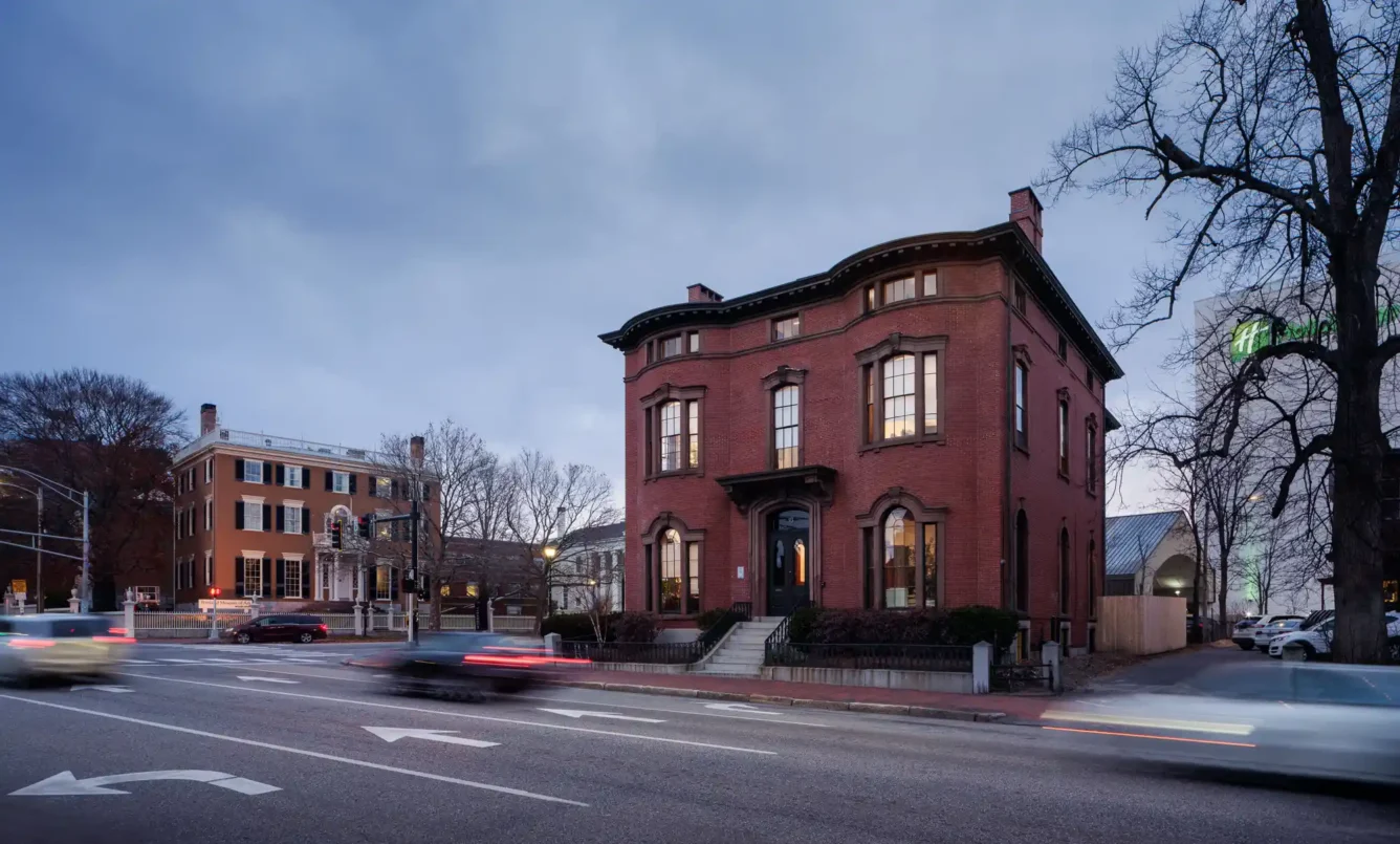 Exterior view of the Safford House at dusk, showcasing the historic brick building with warm lighting highlighting the architectural features.