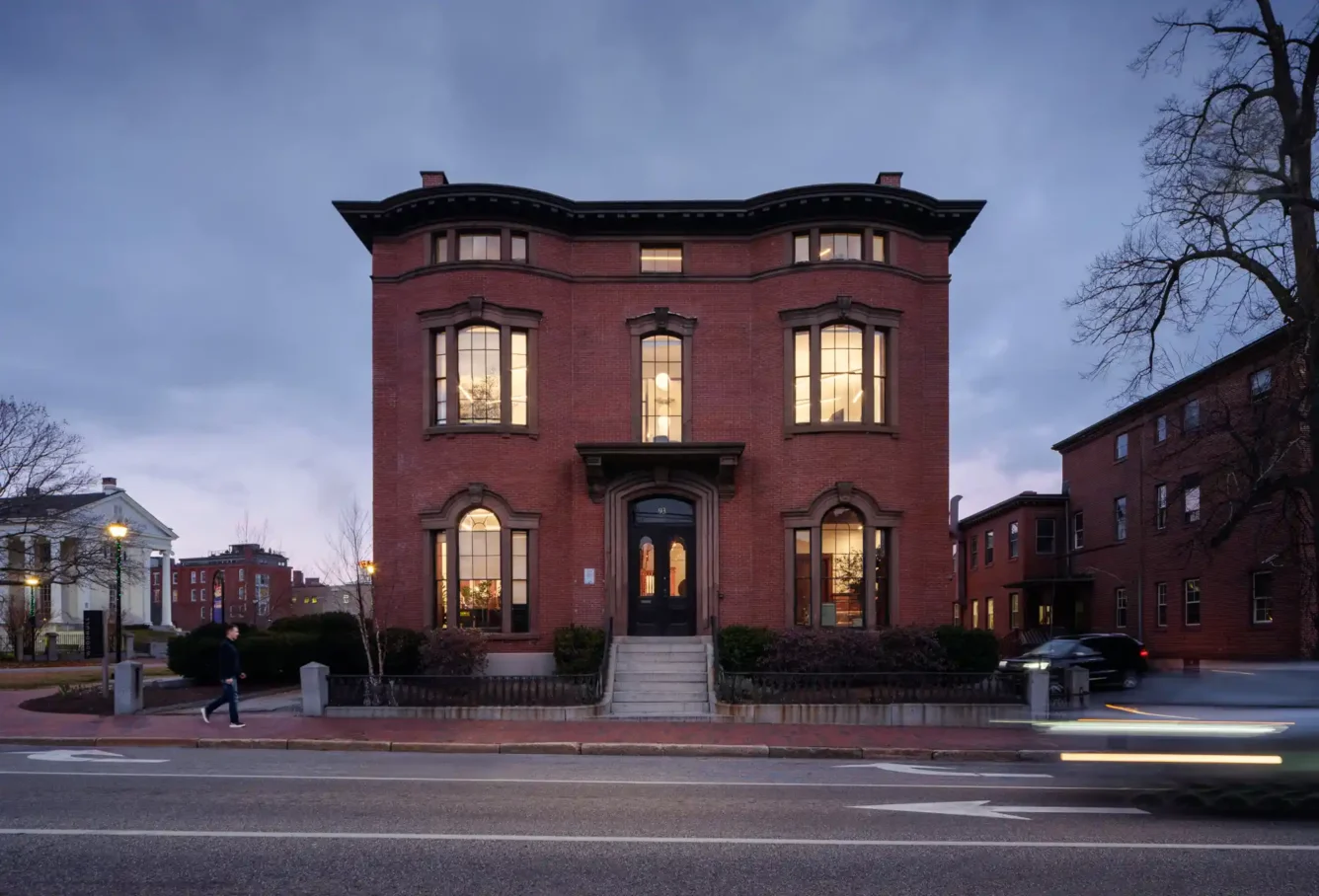 Front view of the Safford House at dusk, with the lights on inside, showcasing the building's brick exterior and historic charm in Portland, Maine.