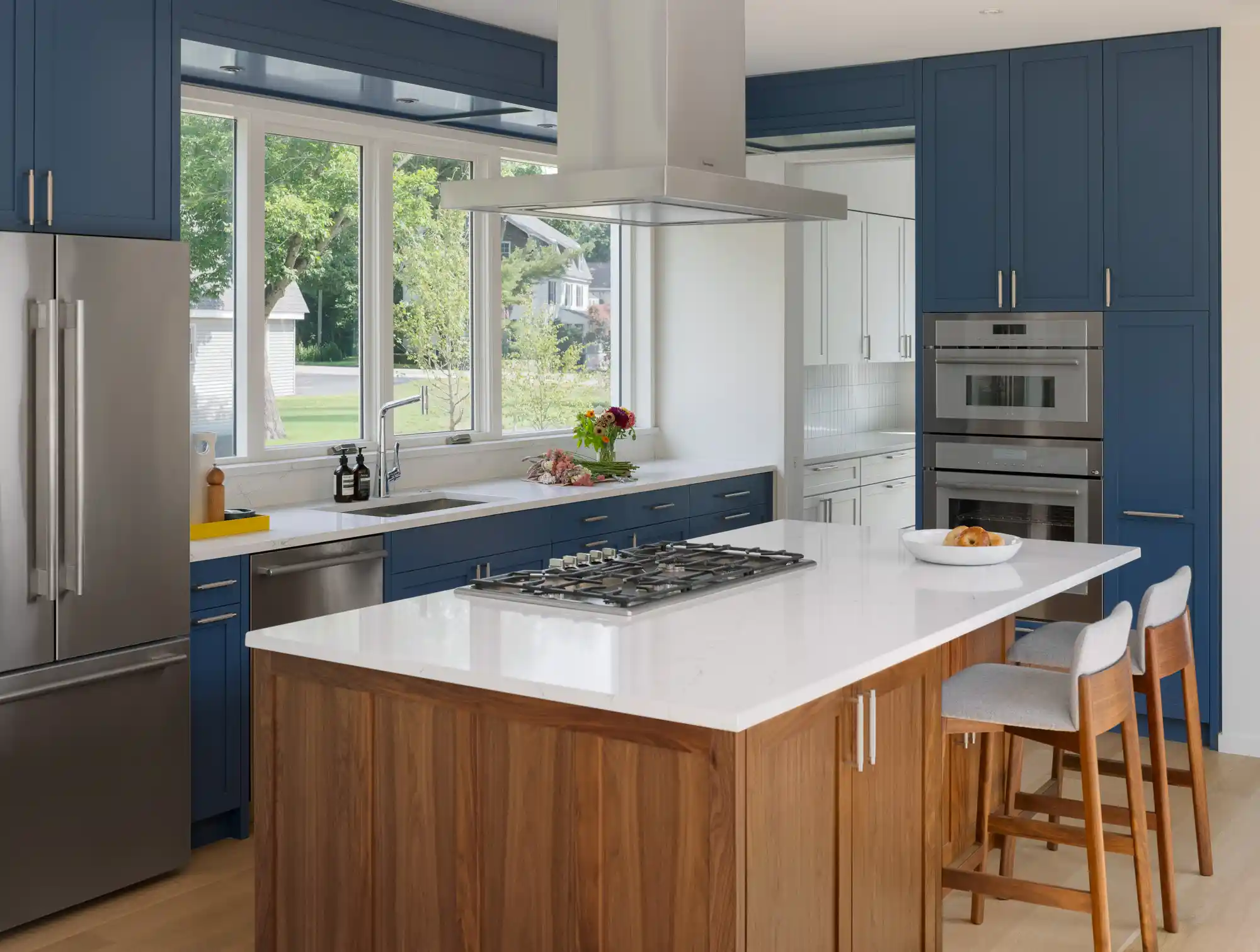 Contemporary kitchen in a custom Woodhull-designed home in Cape Elizabeth, Maine, showcasing blue cabinetry, stainless steel appliances, and a wooden island that adds warmth to the modern design.