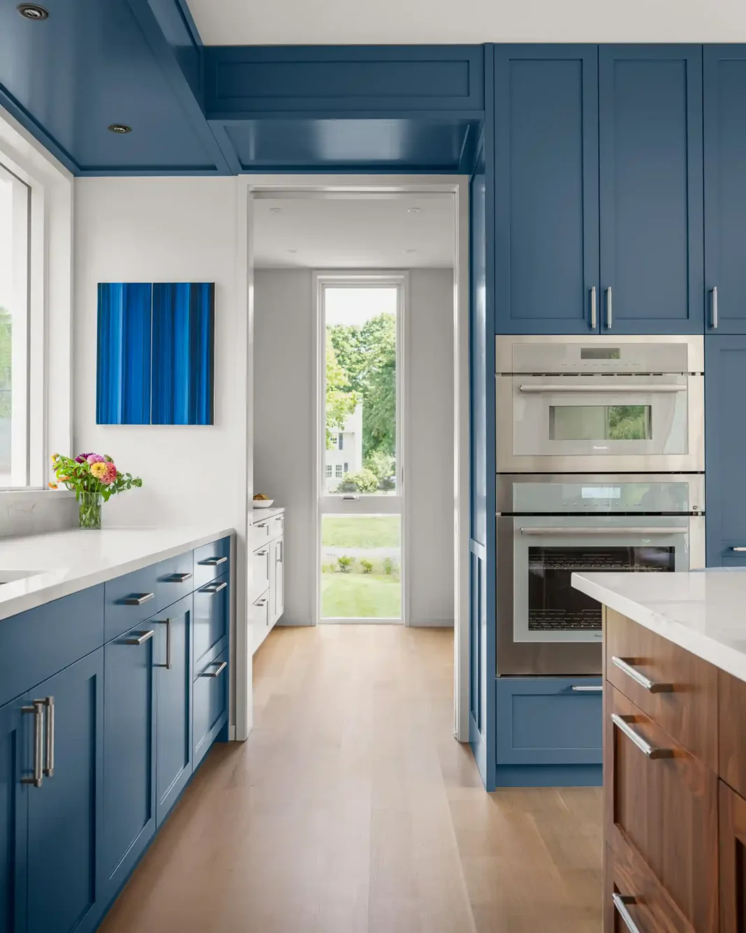 Modern kitchen in a custom home designed by Woodhull in Cape Elizabeth, Maine, featuring blue cabinets, stainless steel appliances, and a wood island for a warm, contemporary look.