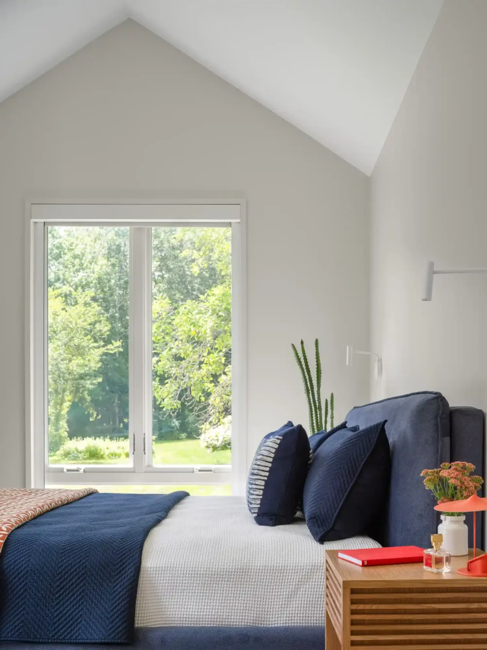 Modern bedroom in a custom home designed by Woodhull in Cape Elizabeth, Maine, featuring a blue fabric headboard, wood nightstand, and natural light creating a bright and serene atmosphere.