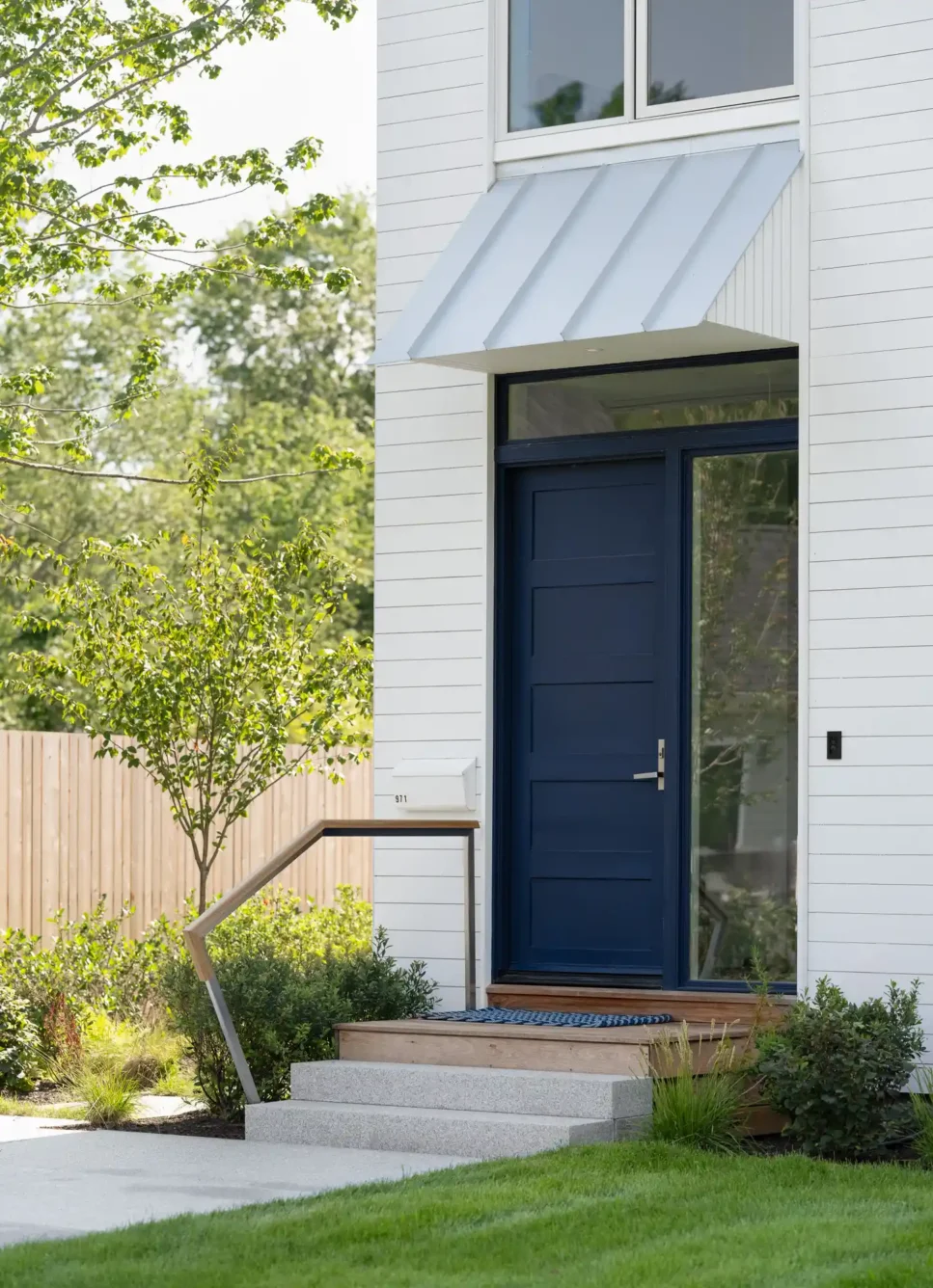 Close-up of the bold blue front door of a modern home in Cape Elizabeth, Maine, designed by Woodhull, highlighting clean lines and white cedar siding.