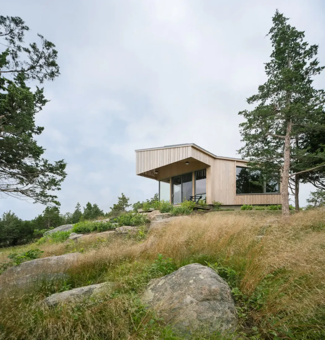 Green Haven’s hillside studio clad in vertical wood siding, nestled among trees and boulders with panoramic views of the coastal landscape