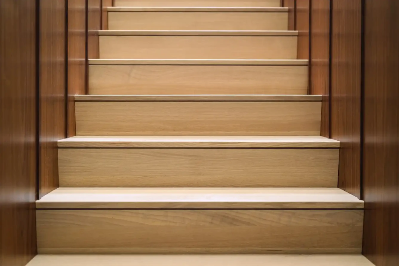 A close-up of an interior staircase featuring sleek light wood steps framed by dark wood-paneled walls. The contrast between materials enhances the modern aesthetic while maintaining a warm and inviting atmosphere.