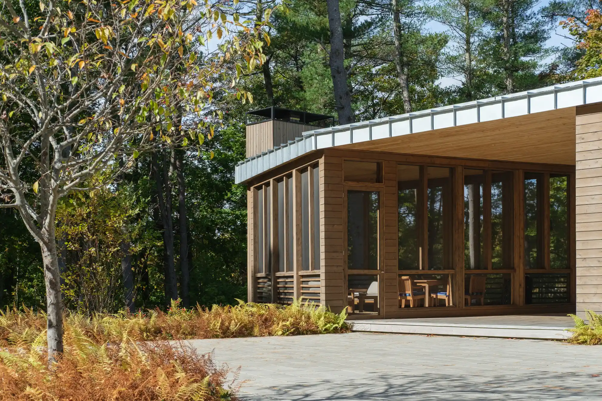 The front view of an enclosed patio, surrounded by woods, stone pathways, and seasonal landscaping in Maine. Large screened openings allow fresh air to flow in while maintaining a cozy and protected space for relaxation.