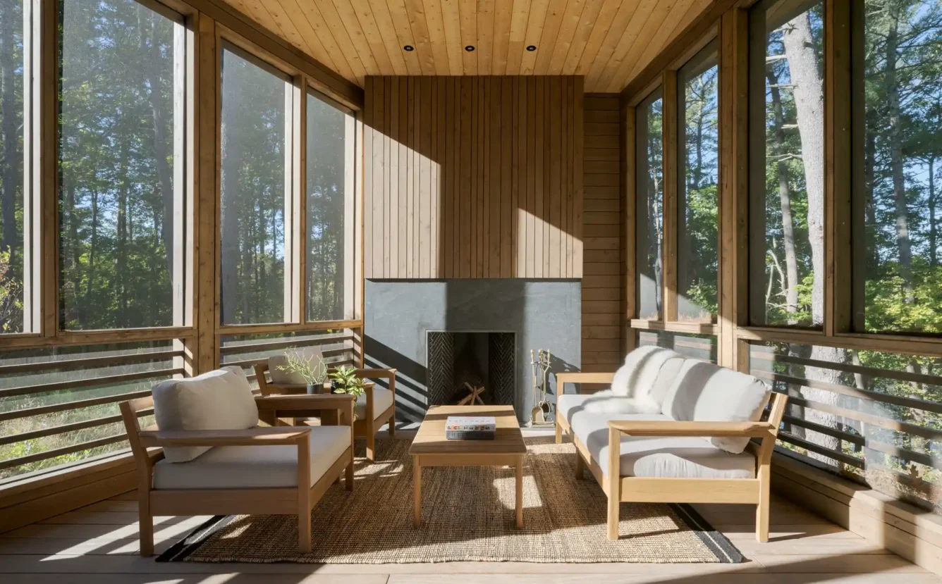 The enclosed patio features warm wood paneling, a sleek dark fireplace, and minimalist modern seating. The design emphasizes a seamless connection between indoor and outdoor living, making it an ideal gathering space.