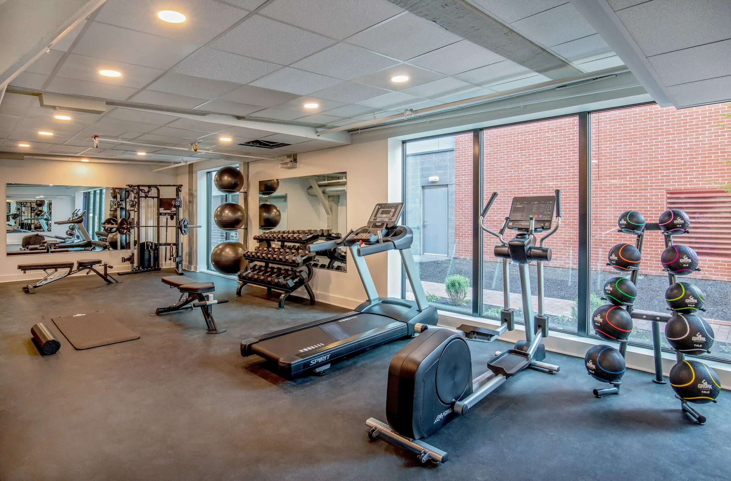 Fitness center at the Weldon Hotel, constructed by Woodhull, featuring treadmills, ellipticals, weight benches, medicine balls, and floor-to-ceiling windows providing natural light