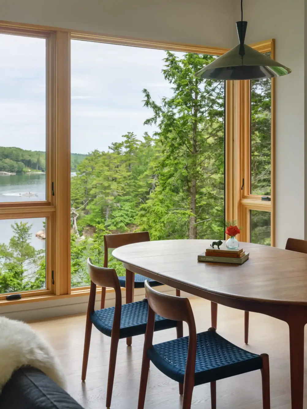 Scenic dining area with wood table, blue chairs, and large window framing river and forest views