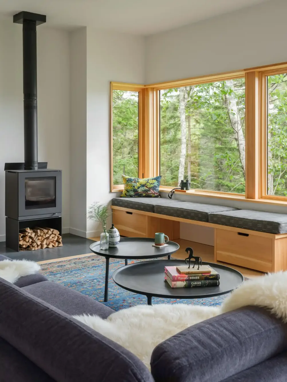 Cozy living room with wood stove, built-in bench, navy sofa, and large windows overlooking forest views