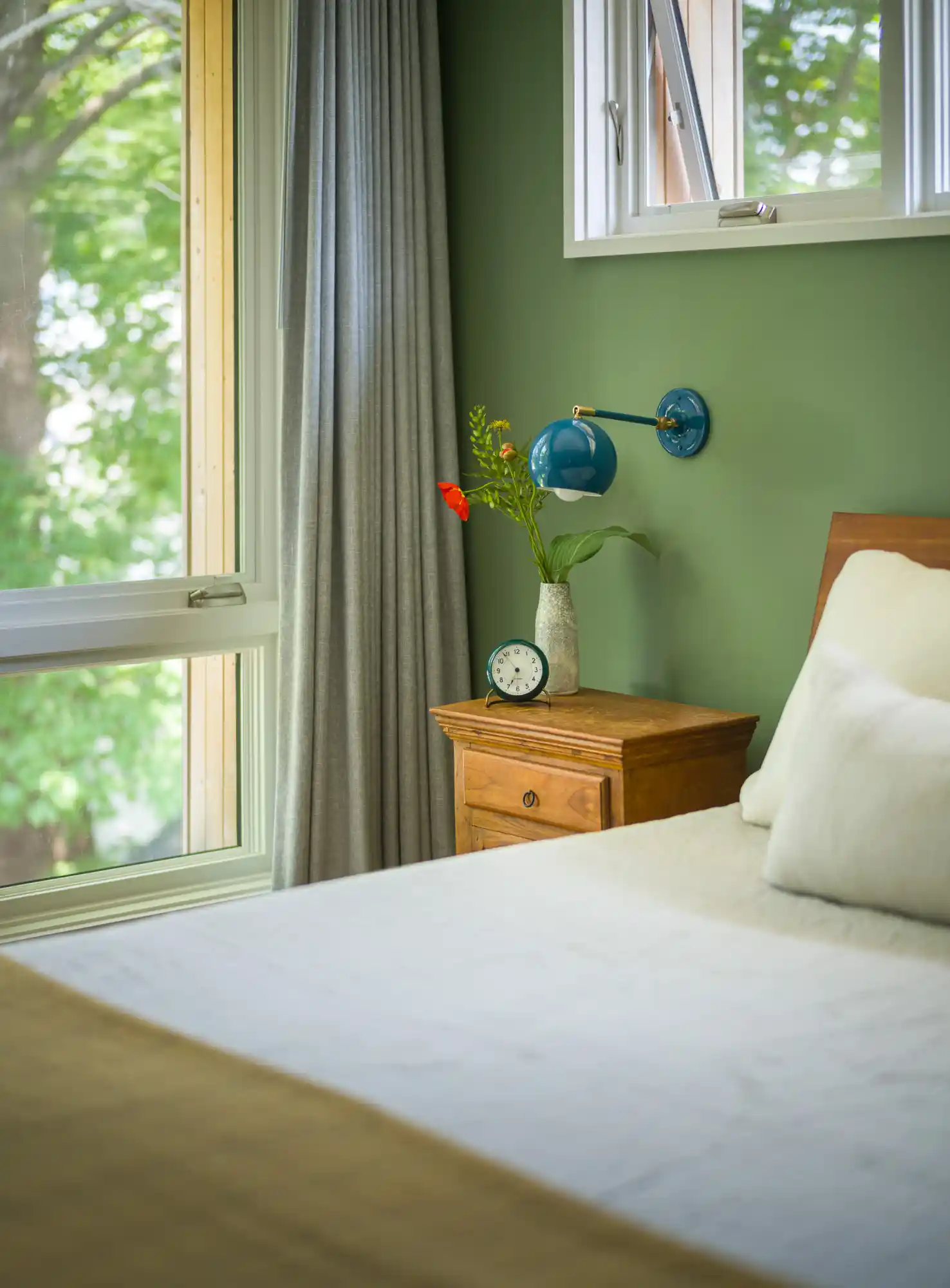 Detail of serene bedroom with wood nightstand, bed, and large window in Willard Cube home