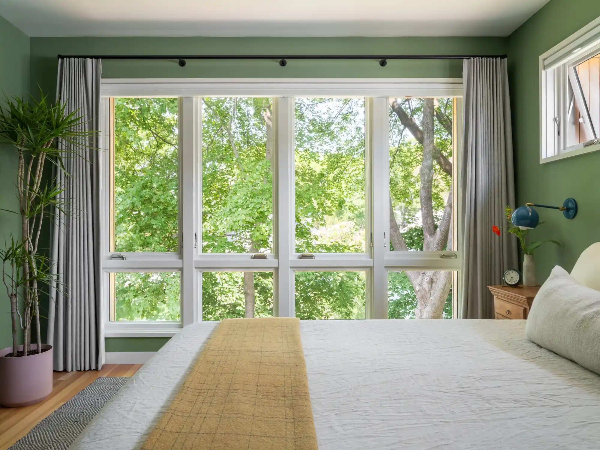 Airy bedroom with green walls, white bedding, and four windows overlooking backyard