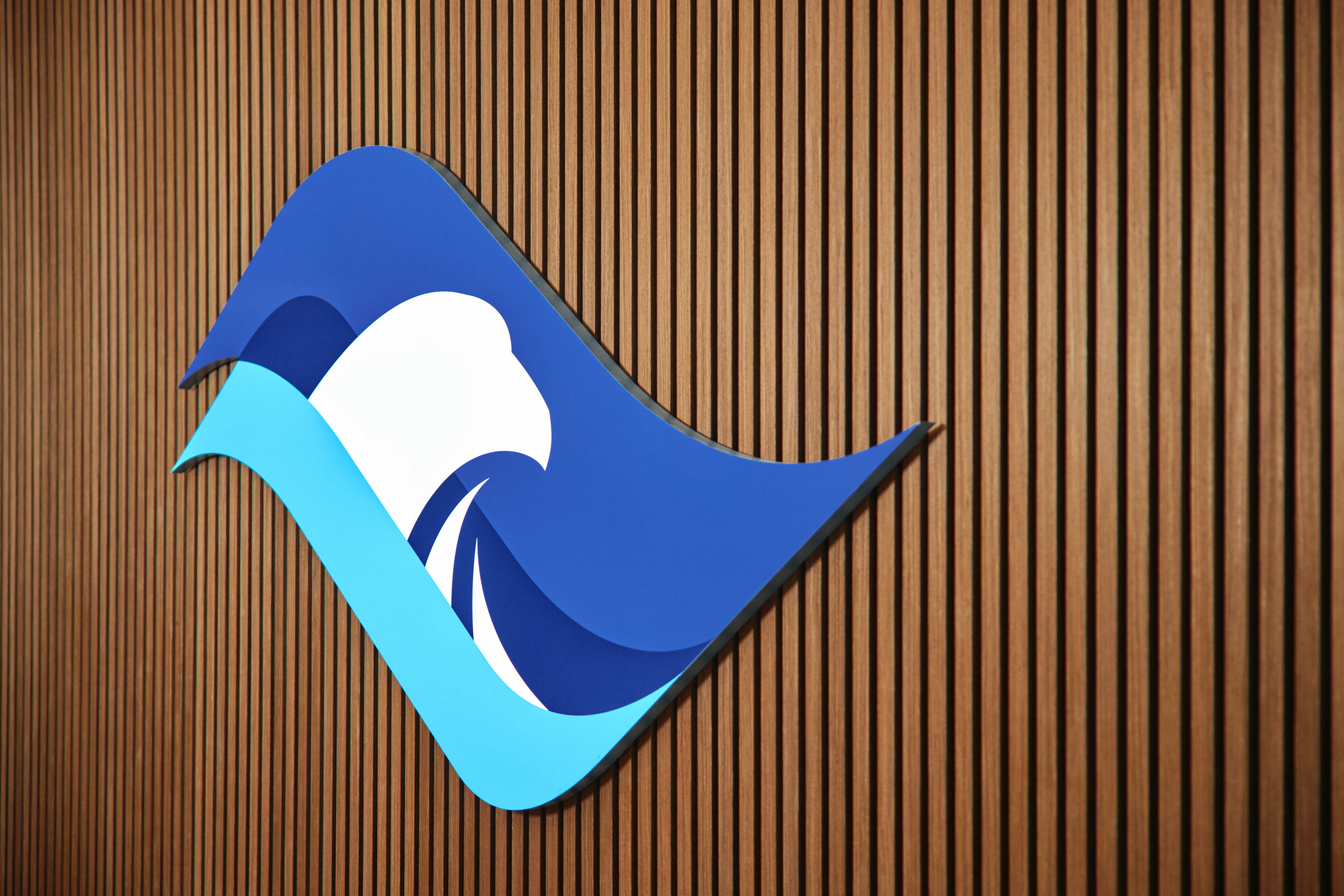 A stylized blue and white eagle logo with wave shapes, mounted on a wall with vertical wooden slats.