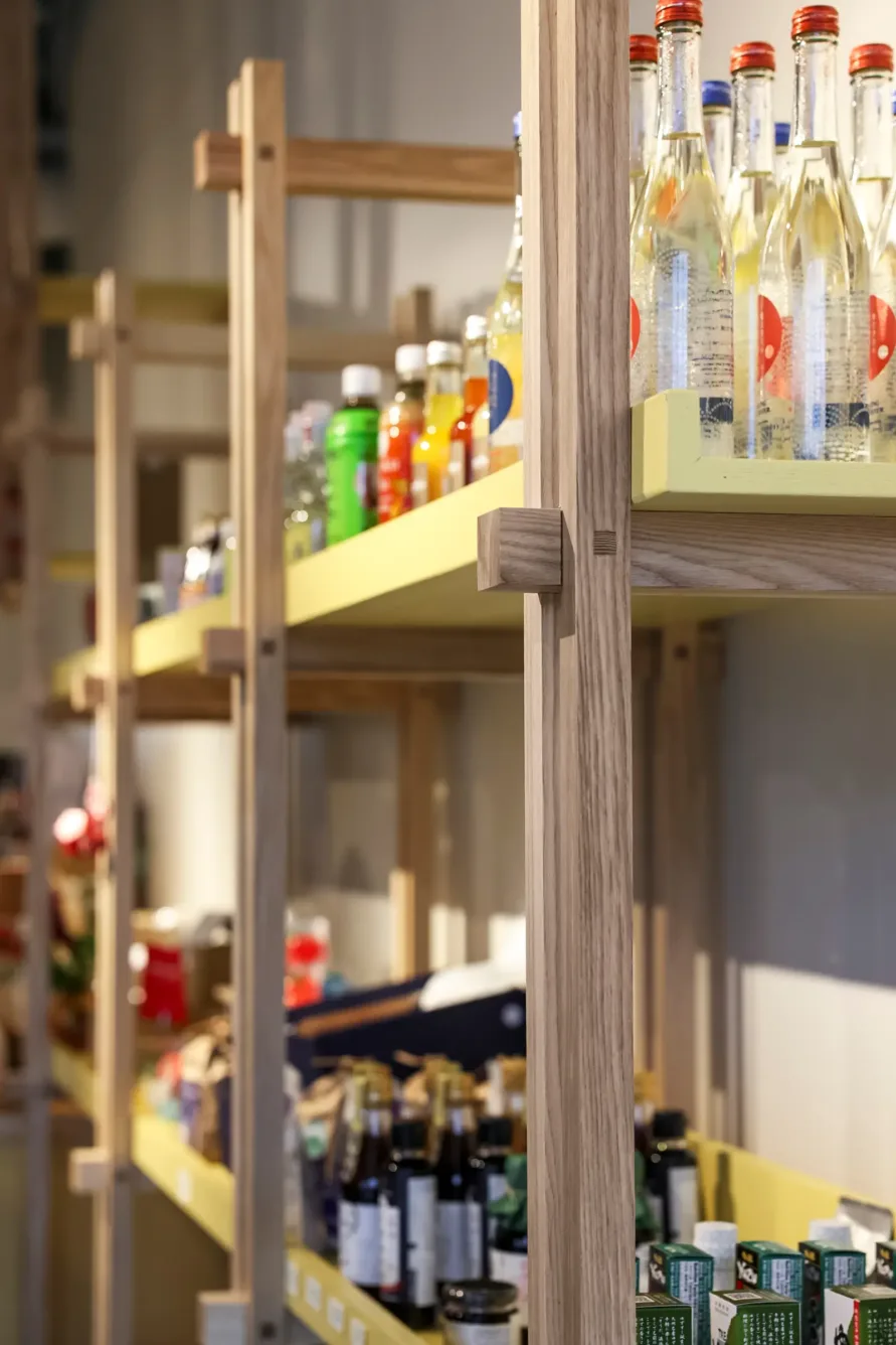 Wooden shelves filled with various bottled drinks and groceries in a store, with items including juices, sodas, and glass water bottles on display.