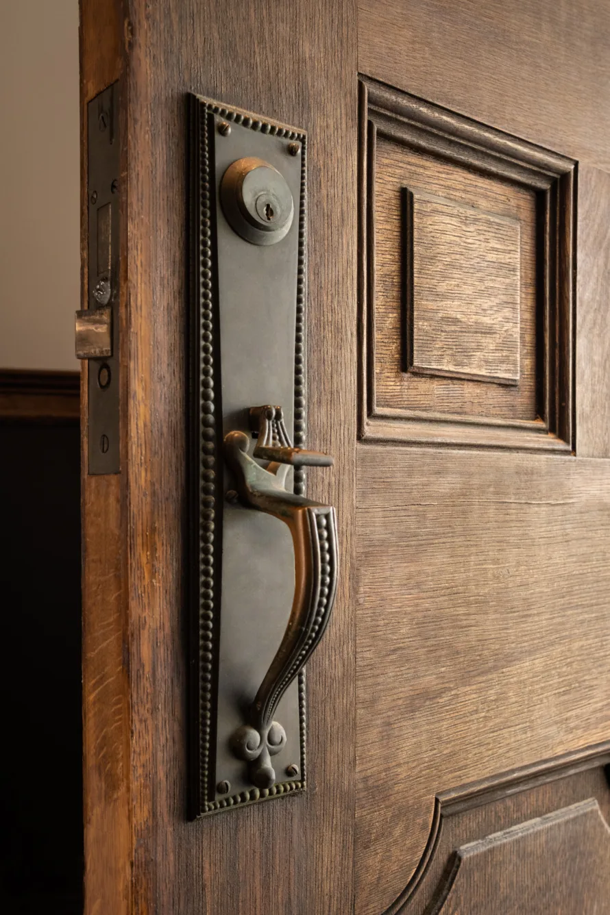 Close-up of an ornate, vintage metal door handle and lock on a partially open wooden door with decorative panels.