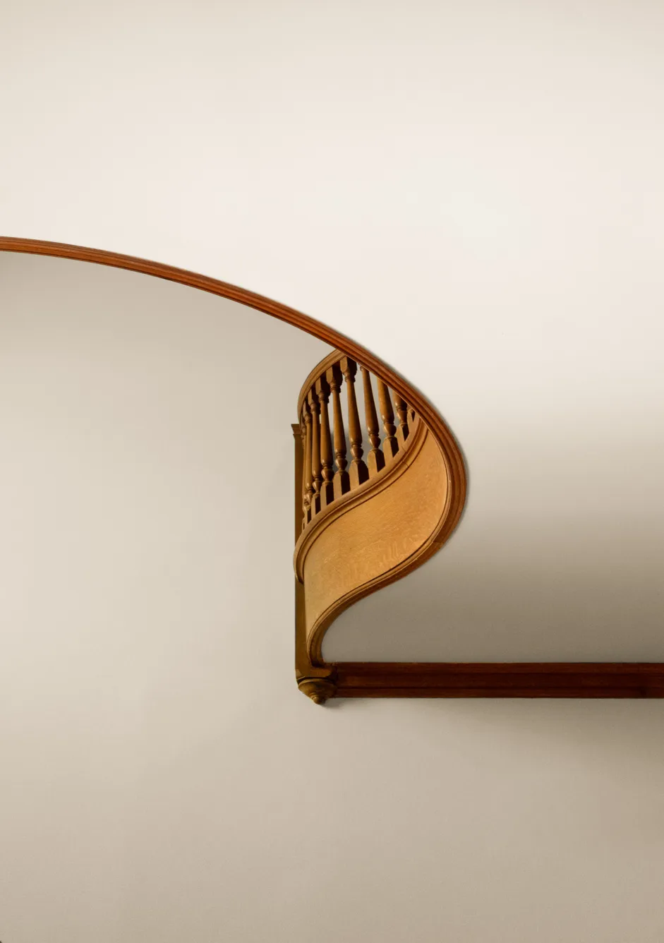 A wooden spiral staircase photographed from below against a plain beige wall, showing elegant curves and balusters.