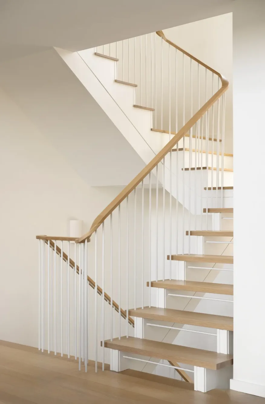 A modern staircase with light wood steps, white vertical railings, and a wooden handrail in a bright, minimalist interior.