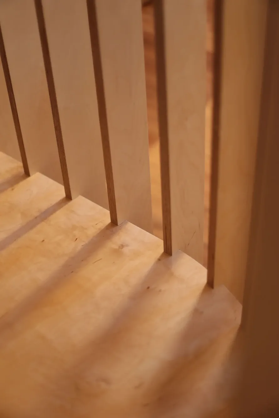 Vertical wooden slats cast shadows on a light wood surface, creating a pattern of light and shadow in a warmly lit indoor setting.