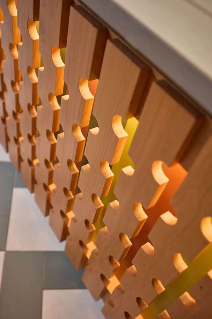 Close-up of a wooden partition with geometric cutouts and warm lighting, next to a patterned tile floor.