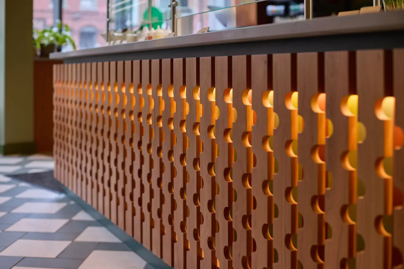 A modern counter with patterned wood paneling and warm backlighting, next to a tiled floor in a restaurant or cafe.