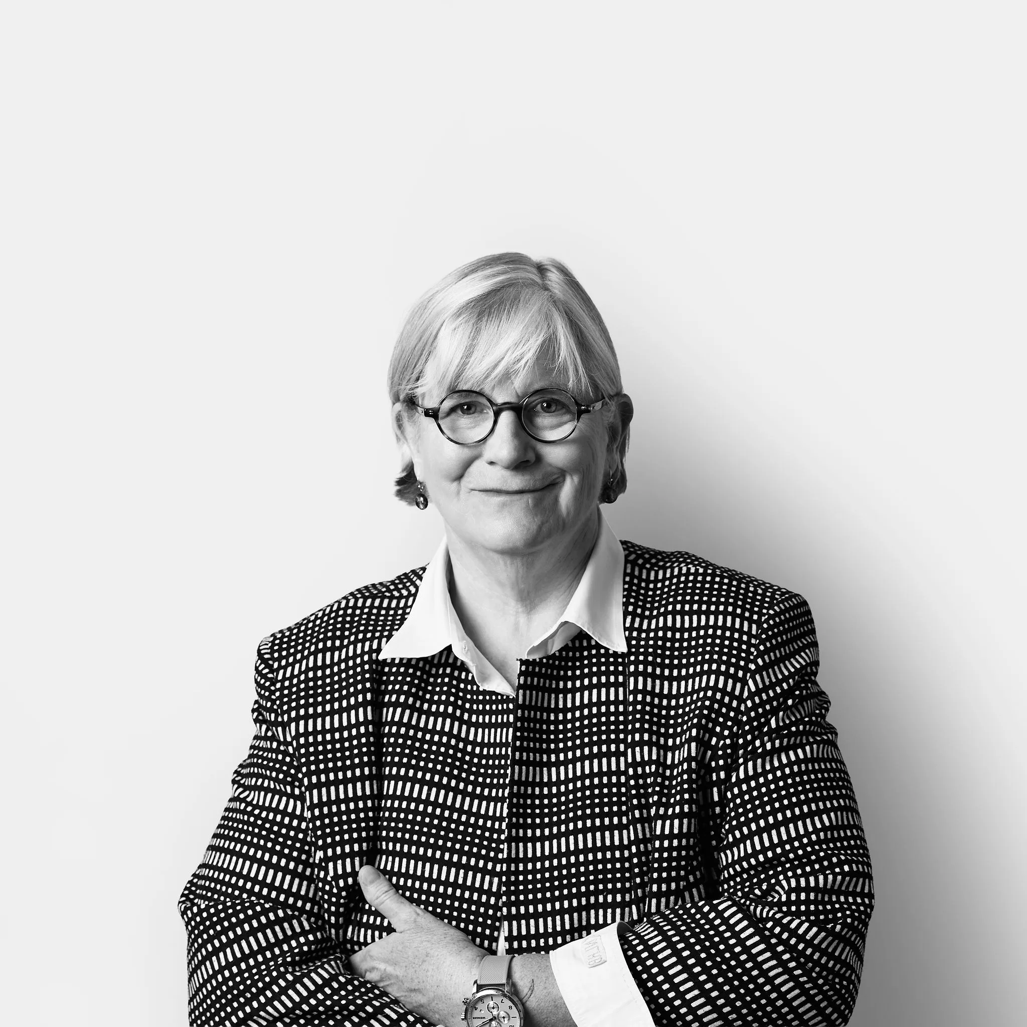 A woman with blonde hair and glasses wears a patterned blazer and smiles at the camera.