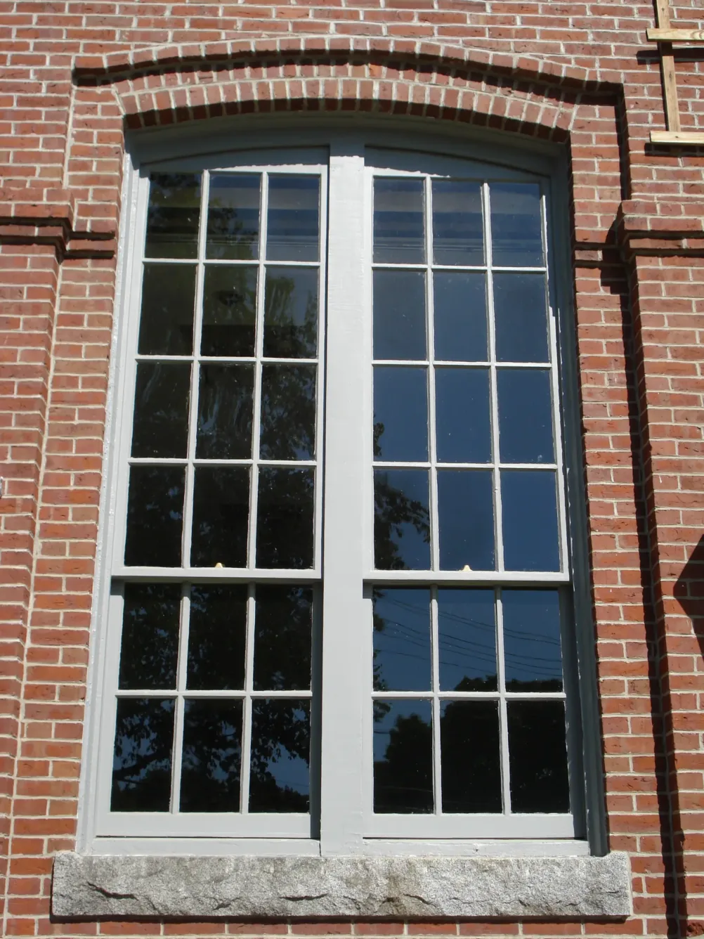 A tall, double-pane window with a grid of panes set into a red brick wall.